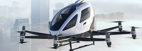 A white passenger drone with four arms and eight rotors flies above a city skyline in foggy weather.
