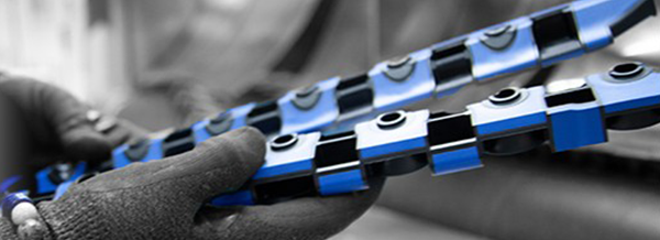 A gloved hand holds two blue and black segmented plastic strips, possibly machine parts, in a workshop setting.