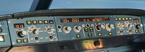 Close-up of an aircraft cockpit control panel showing various switches, knobs, digital displays, and indicator lights.