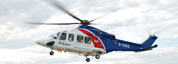 A blue, white, and red helicopter with Bristow and G-CKKQ markings flies against a cloudy sky.