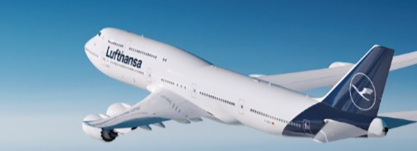 A Lufthansa aeroplane flies through a clear blue sky, viewed from the side with its logo visible on the tail and fuselage.