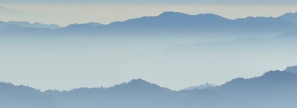 Layers of blue misty mountains fade into the distance under a soft, pale sky.